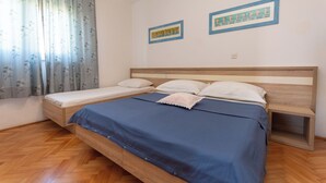 A bedroom with a wooden bed, a blue bedspread, a wooden nightstand, and two framed pictures on the wall. - Apartments Jadranka sea View (Novalja)