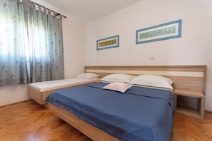 A bedroom with a wooden bed, a blue bedspread, a wooden nightstand, and two framed pictures on the wall. - Apartments Jadranka sea View (Novalja)