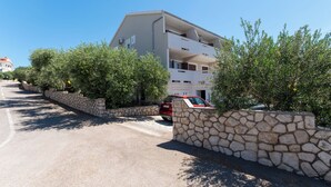 A modern two-story building with a stone wall and greenery in front. - Apartments Jadranka sea View (Novalja)