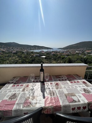 Ein Tisch mit einer Flasche und Gläsern, mit Blick auf eine Küstenstadt und Hügel.