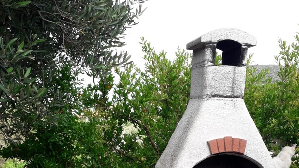 Forno a pizza de tijolo e betão com chaminé, assente numa plataforma de betão com pavimento em mosaico.