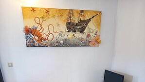 Uma sala de estar com um sofá laranja, uma TV de tela plana em um suporte e um quadro pendurado na parede.