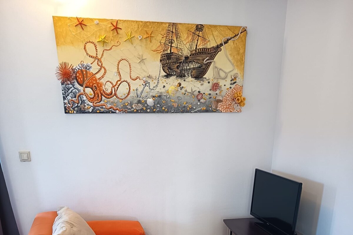 A living room with an orange sofa, a flat-screen TV on a stand, and a wall-mounted painting.