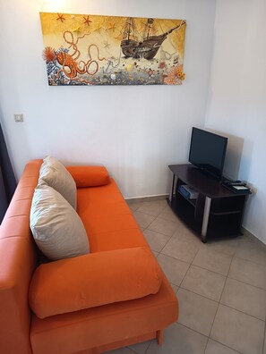 A living room with an orange sofa, a flat-screen TV on a stand, and a wall-mounted painting. - Apartments Stipan (Marina)