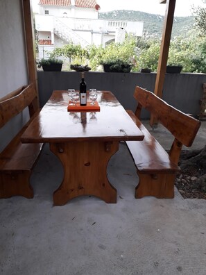 Ein Holztisch mit Bänken, einer Weinflasche und Gläsern auf einem Balkon.