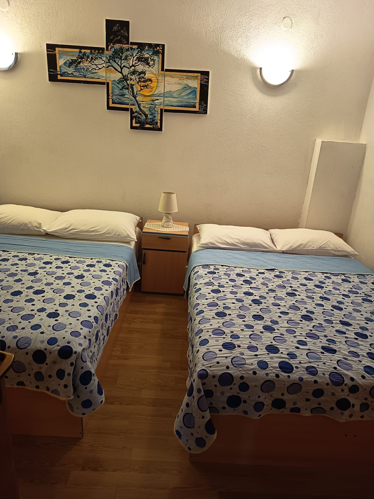 A room with two beds, a nightstand with a lamp, and wall art.