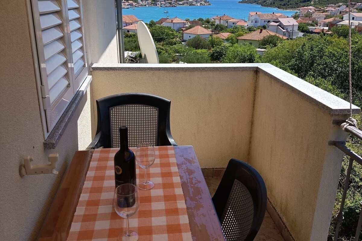 A balcony with a table, chairs, and a view of a coastal town.