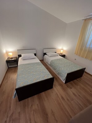 Ein Doppelzimmer mit zwei Einzelbetten, Holzboden, Nachttische mit Lampen und ein Fenster mit Vorhängen.