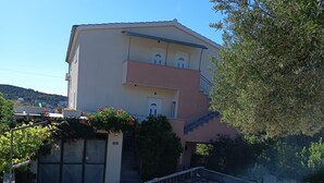 Um edifício de vários andares com telhado plano, uma escadaria que leva à entrada e um pátio pavimentado.