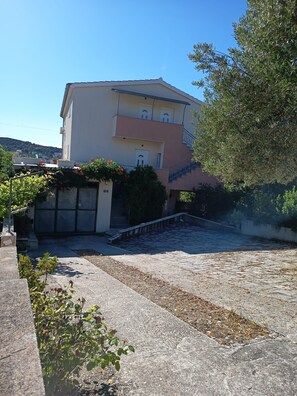A multi-story building with a flat roof, a staircase leading to the entrance, and a paved courtyard. - Apartments Stipan (Marina)