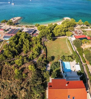 Vista aérea de una propiedad costera con paneles solares, piscina y playa.