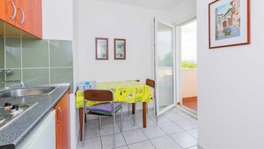 Eine kleine Küche mit Spüle, einem Tisch mit Stühlen und einem Balkon mit Glastür.