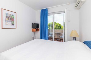 Una habitación de hotel con cama, televisión, balcón con mesa y sillas, y una lámpara.
