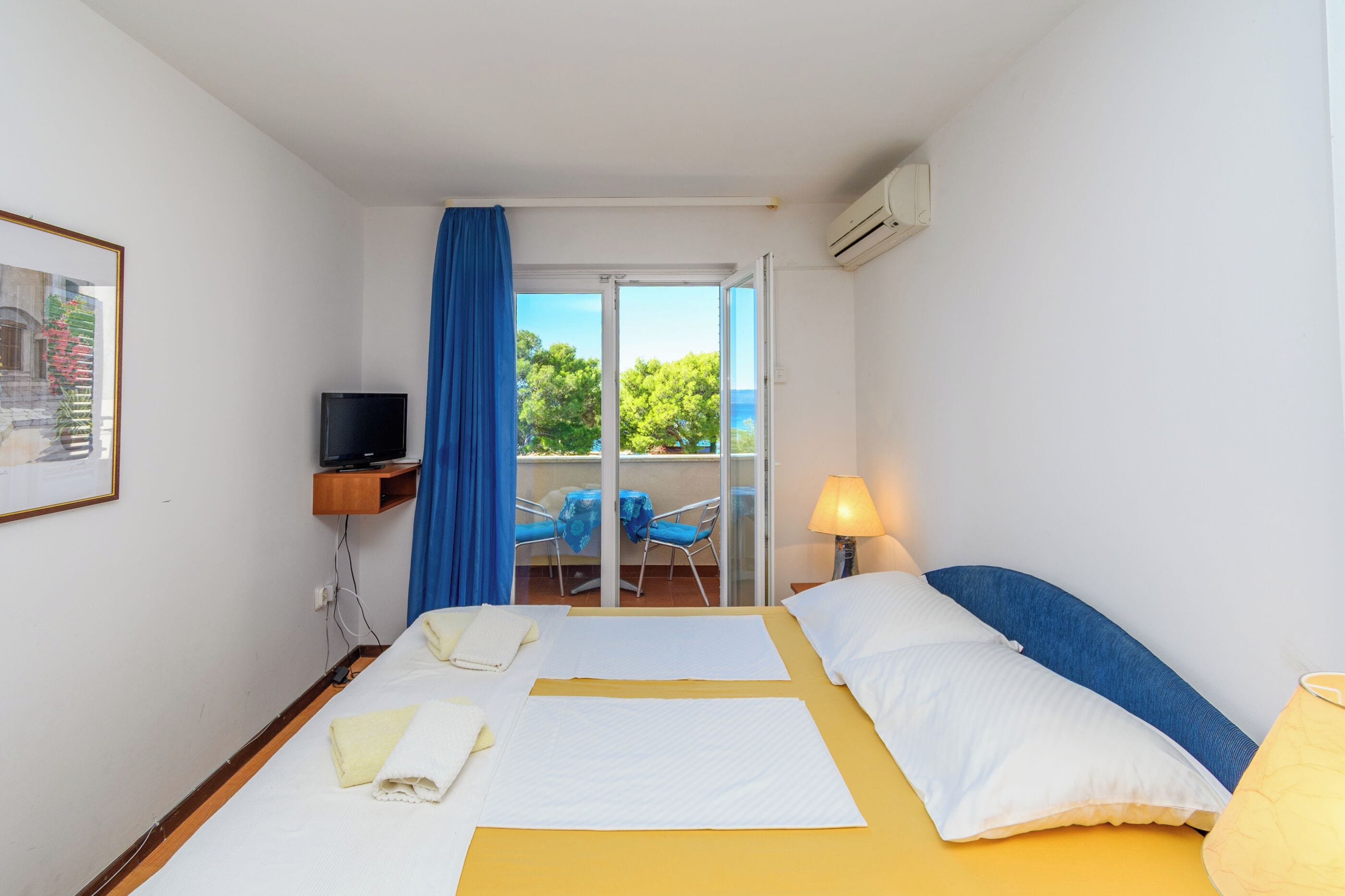 Ein Hotelzimmer mit Bett, Fernseher, Balkon mit Stühlen und Blick auf Grünflächen.
