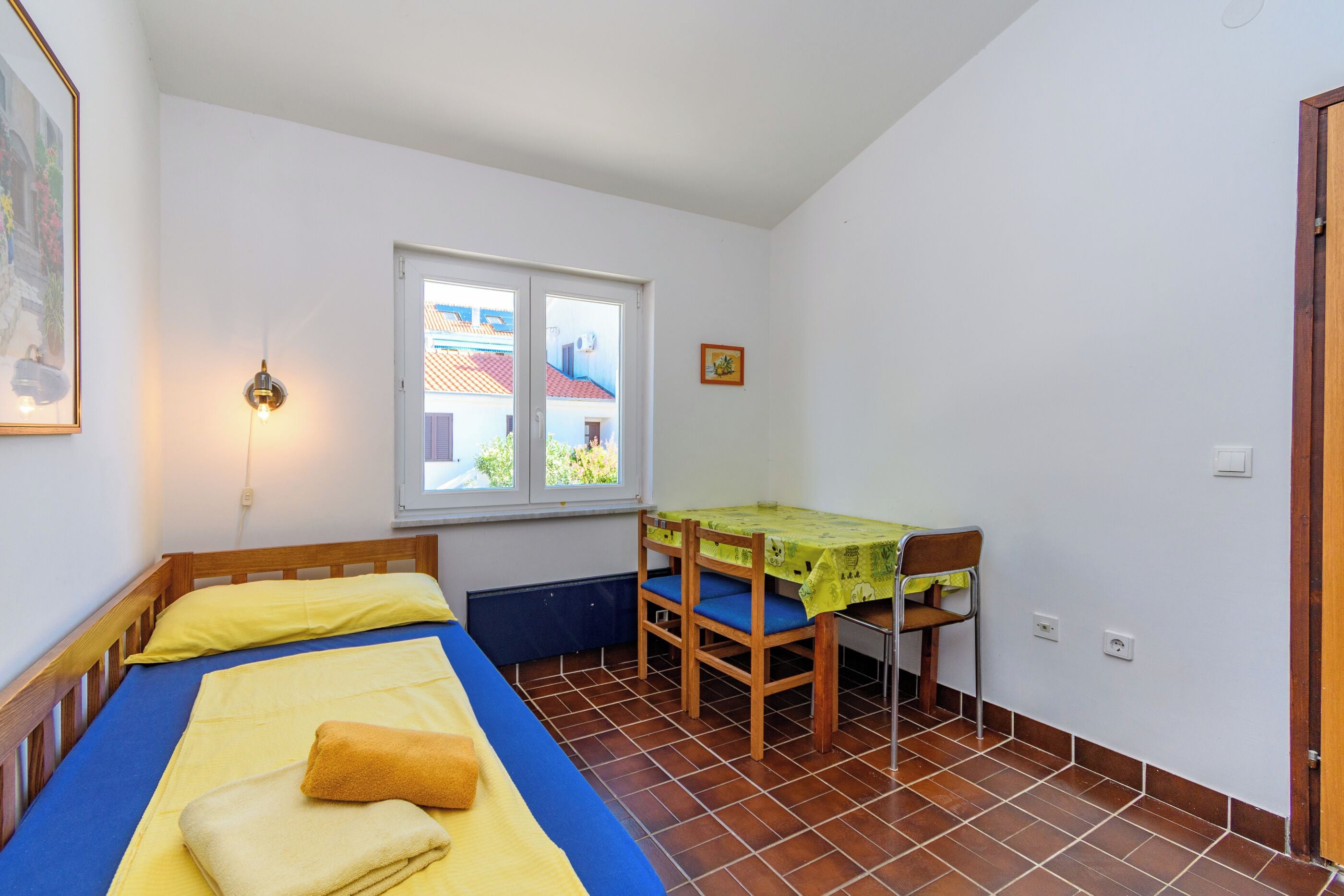 Une petite pièce avec deux lits, une table avec des chaises, une fenêtre et une porte.