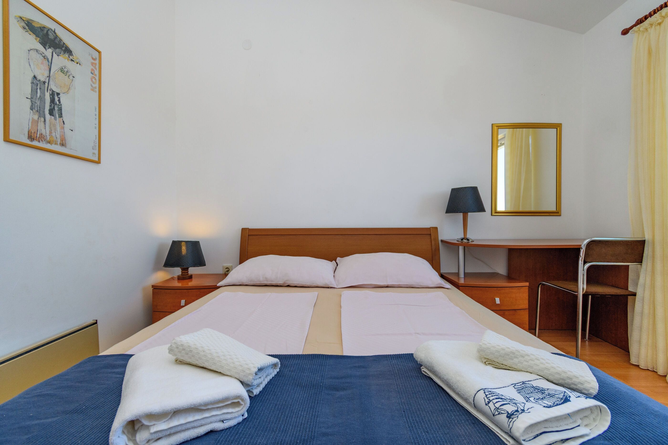 A hotel room with a double bed, a desk, a chair, a lamp, and a mirror.