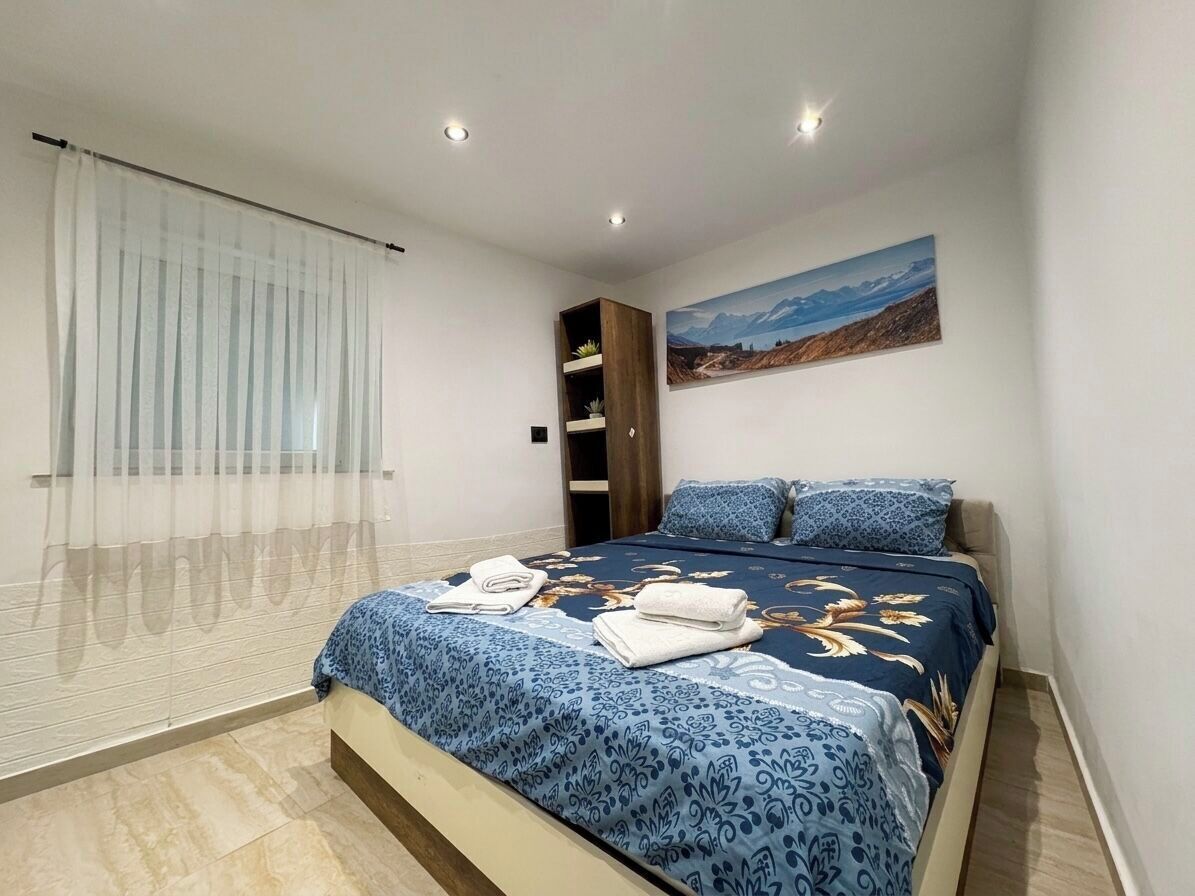 Une chambre à coucher avec un lit, une fenêtre ornée de rideaux légers, un tableau accroché au mur et une étagère intégrée.