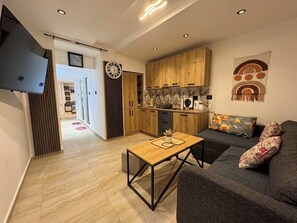 A modern living room with a sofa, a coffee table, and a kitchen area with wooden cabinets and a TV. - House Holiday House Art (Crikvenica)