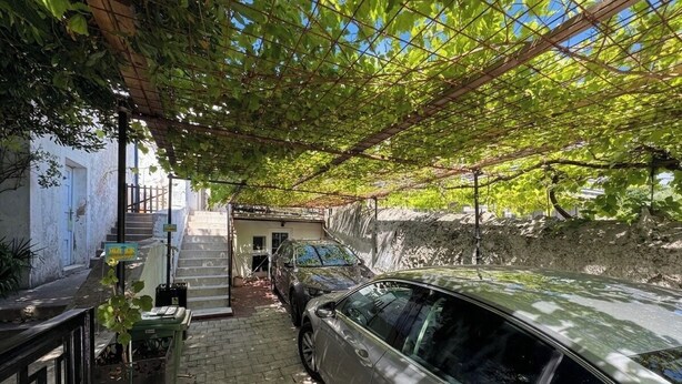A narrow driveway with a parked car, a staircase leading to a building, and a pergola with vines overhead. - House Holiday House Art (Crikvenica)