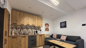A modern kitchen with wooden cabinets, a dining area with a sofa and a coffee table, and a wall with abstract art. - House Holiday House Art (Crikvenica)