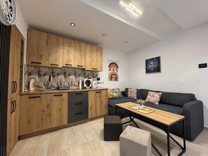 A modern kitchen with wooden cabinets, a dining area with a sofa and a coffee table, and a wall with abstract art. - House Holiday House Art (Crikvenica)