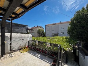 A balcony with a metal bicycle rack, a potted plant, and a view of neighboring buildings. - House Holiday House Art (Crikvenica)