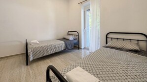 A bedroom with two beds, a window with curtains, an air conditioning unit, and a door. - House Holiday House Art (Crikvenica)
