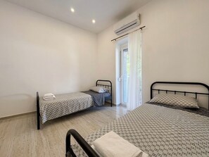 A bedroom with two beds, a window with curtains, an air conditioning unit, and a door. - House Holiday House Art (Crikvenica)