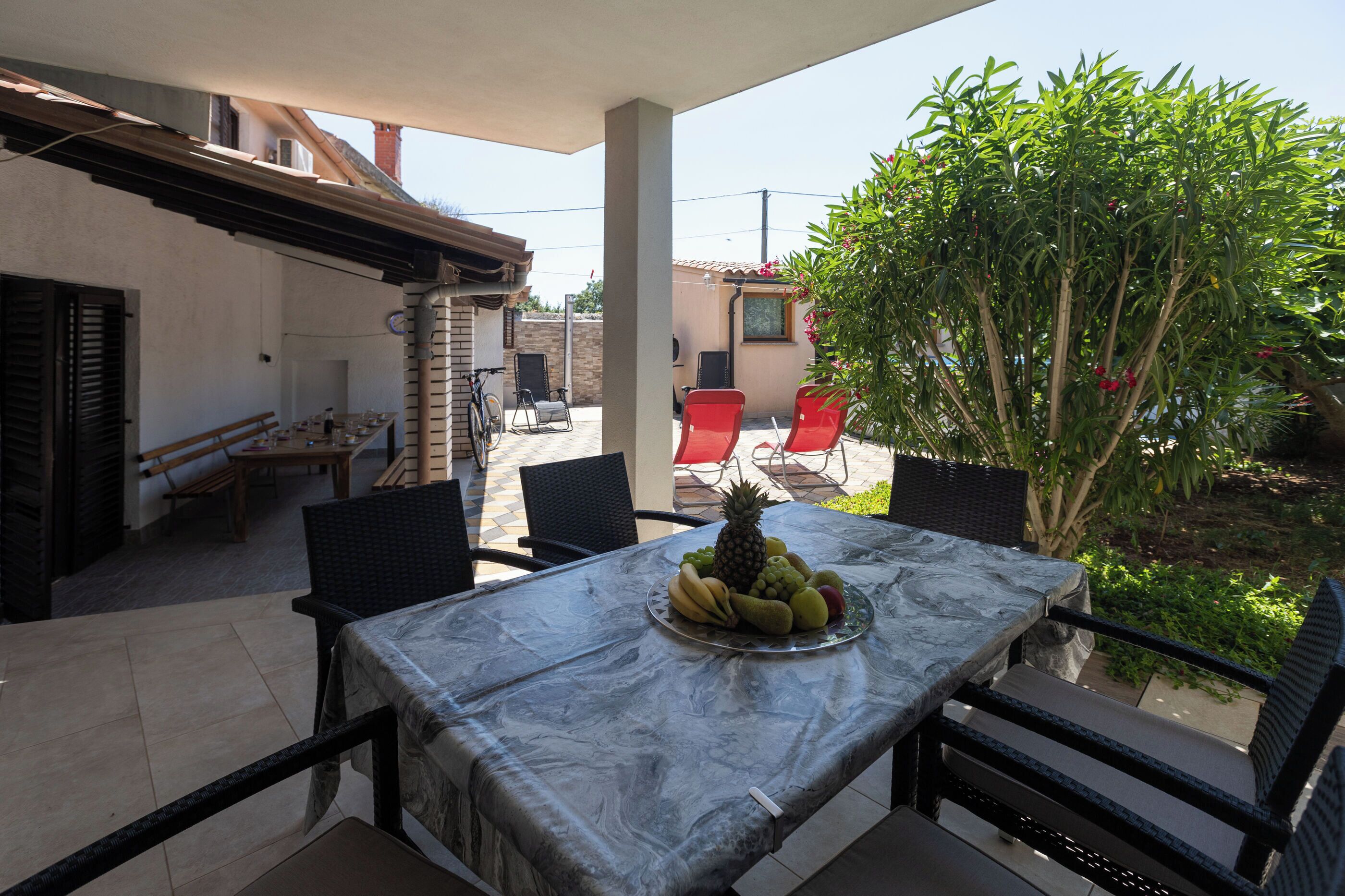 A patio with a table set for two, a fruit platter, and a view of a garden.