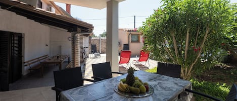 A patio with a table set for two, a fruit platter, and a view of a garden.