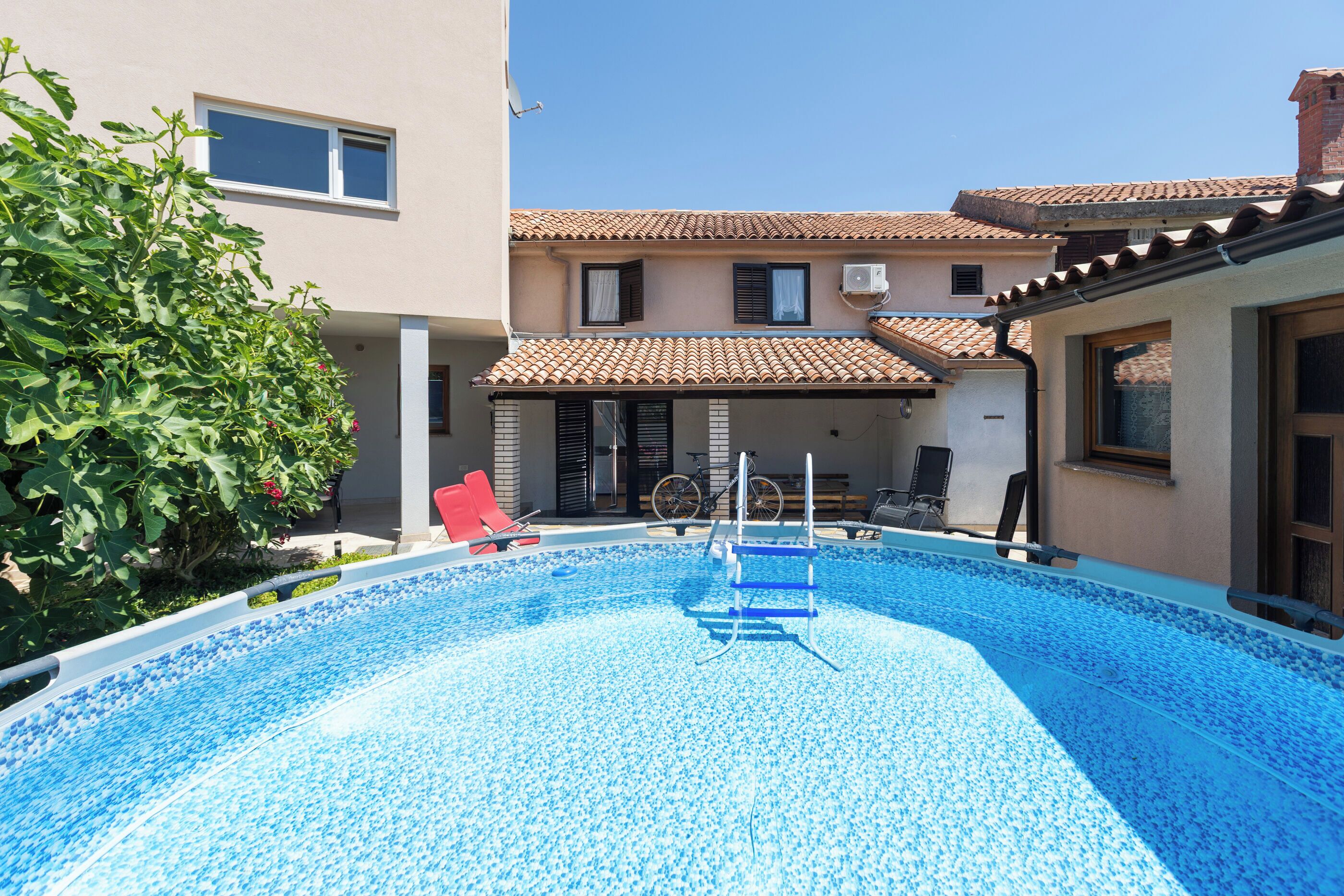 A swimming pool with a blue tiled deck, a red lounge chair, and a bicycle parked outside.