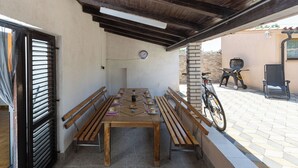 An outdoor patio with a wooden table, benches, a bicycle, and a grill. - House Bakic (Marcana)