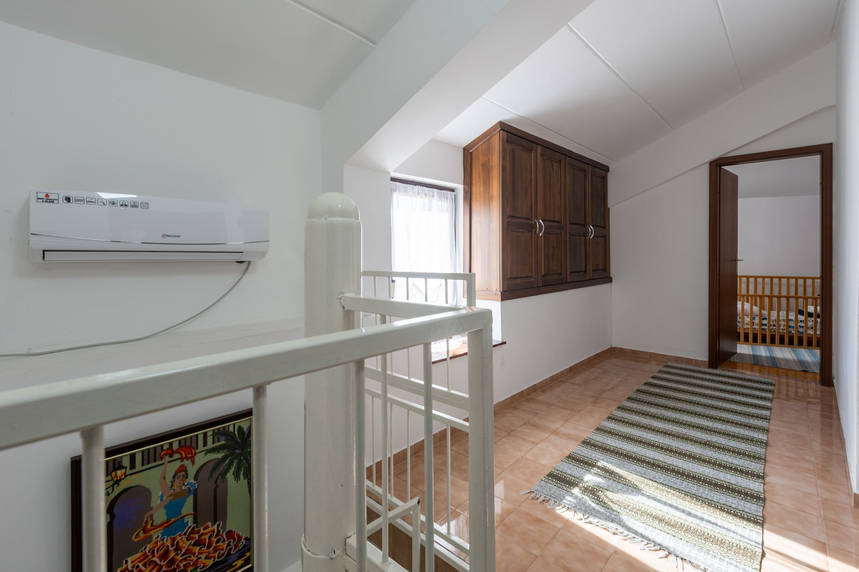 Ein Zimmer mit Klimaanlage, Holzschrank, gestreiftem Teppich und weißer Geländer.