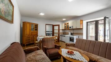 A living room with a sofa, armchair, dining table, and kitchen area with cabinets and appliances.