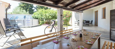 An outdoor patio with a table set for dining, a bicycle, and a view of the street and greenery.