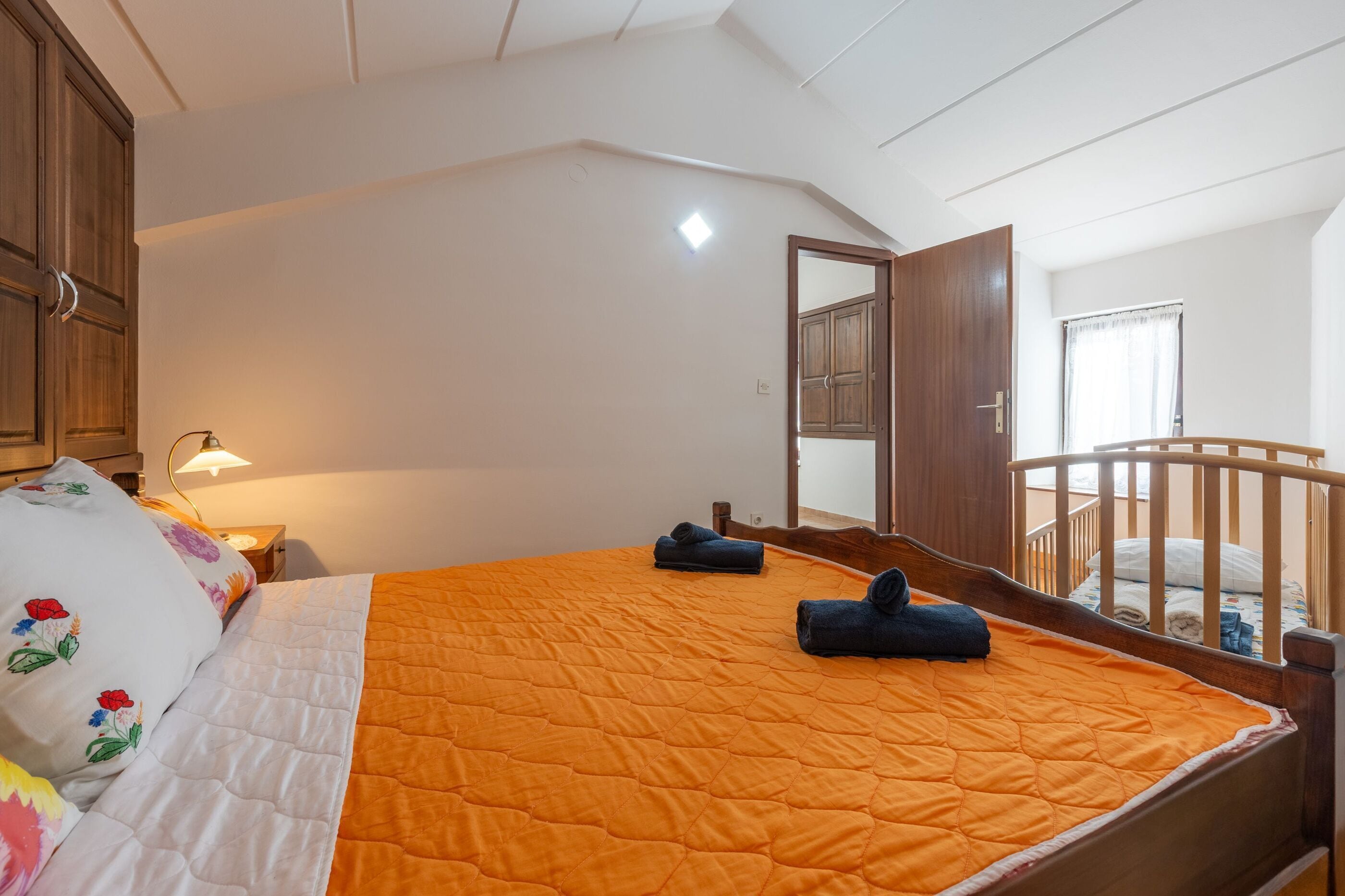 Un dormitorio con cama, mesita de noche, lámpara, armario de madera y vistas a un balcón.