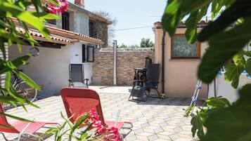 A patio with a red chair, a table, a grill, and a bicycle.