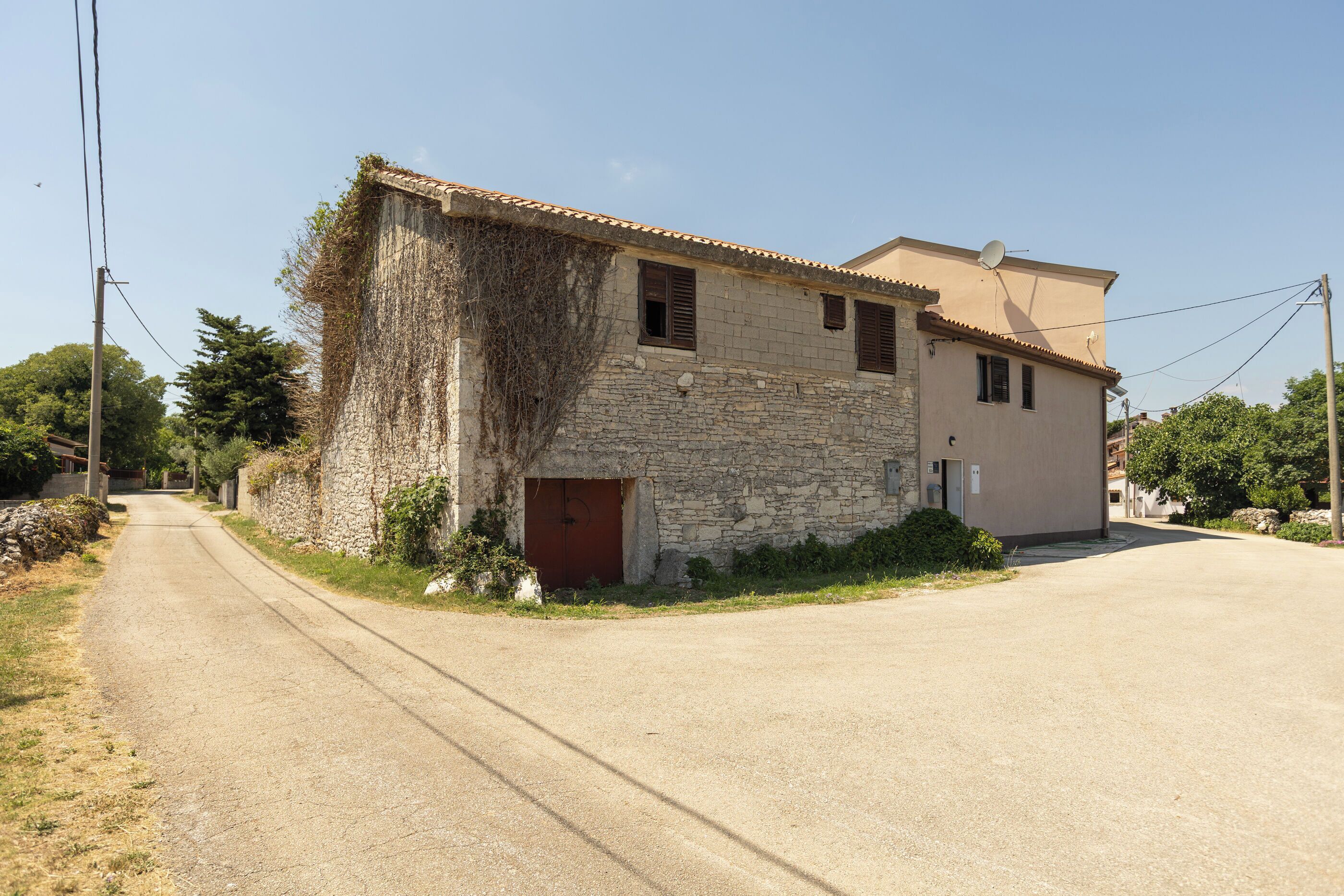 A two-story stone building with a red door, a satellite dish, and a paved road in front.