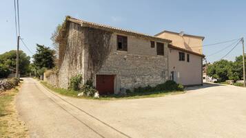A two-story stone building with a red door, a satellite dish, and a paved road in front.