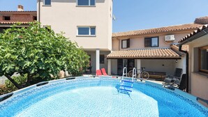 A swimming pool with a ladder, lounge chairs, and a building with a tiled roof. - House Bakic (Marcana)