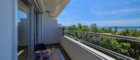 A balcony with a table, chairs, and a view of the sea and greenery.