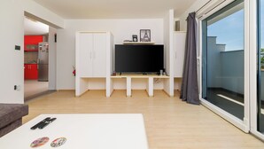Ein modernes Wohnzimmer mit Flachbildfernseher, einem weißen Sofa und einem Esstisch.
