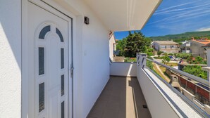 Ein Balkon mit weißer Tür, freier Blick auf die Nachbarschaft und einem Metallgeländer.