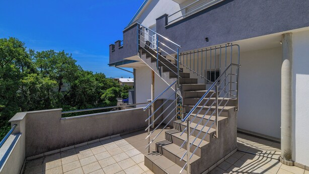 Ein modernes Gebäude mit einer Treppe, die zu einer oberen Ebene führt, umgeben von Grünflächen.