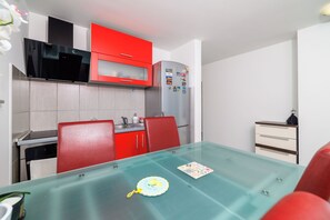 A compact kitchen with red cabinets, a stainless steel refrigerator, and a glass dining table. - Apartment Evelin (Crikvenica)