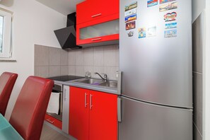 A kitchen with red cabinets, a stainless steel refrigerator, a sink, and a window. - Apartment Evelin (Crikvenica)