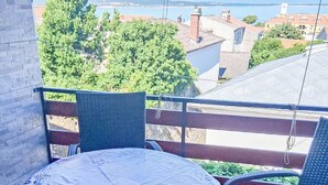 Ein Balkon mit rundem Tisch und Korbstühlen, der auf einen Wohnbereich und ein Gewässer blickt.