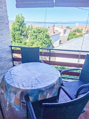 Ein Balkon mit rundem Tisch und Korbstühlen, der auf einen Wohnbereich und ein Gewässer blickt.