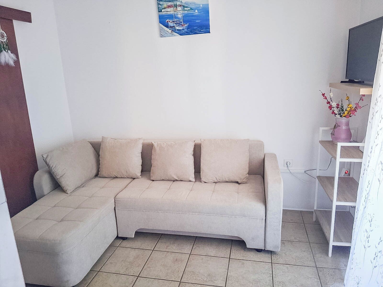 A living room with a sofa, a television, and a wall-mounted shelf with a vase.