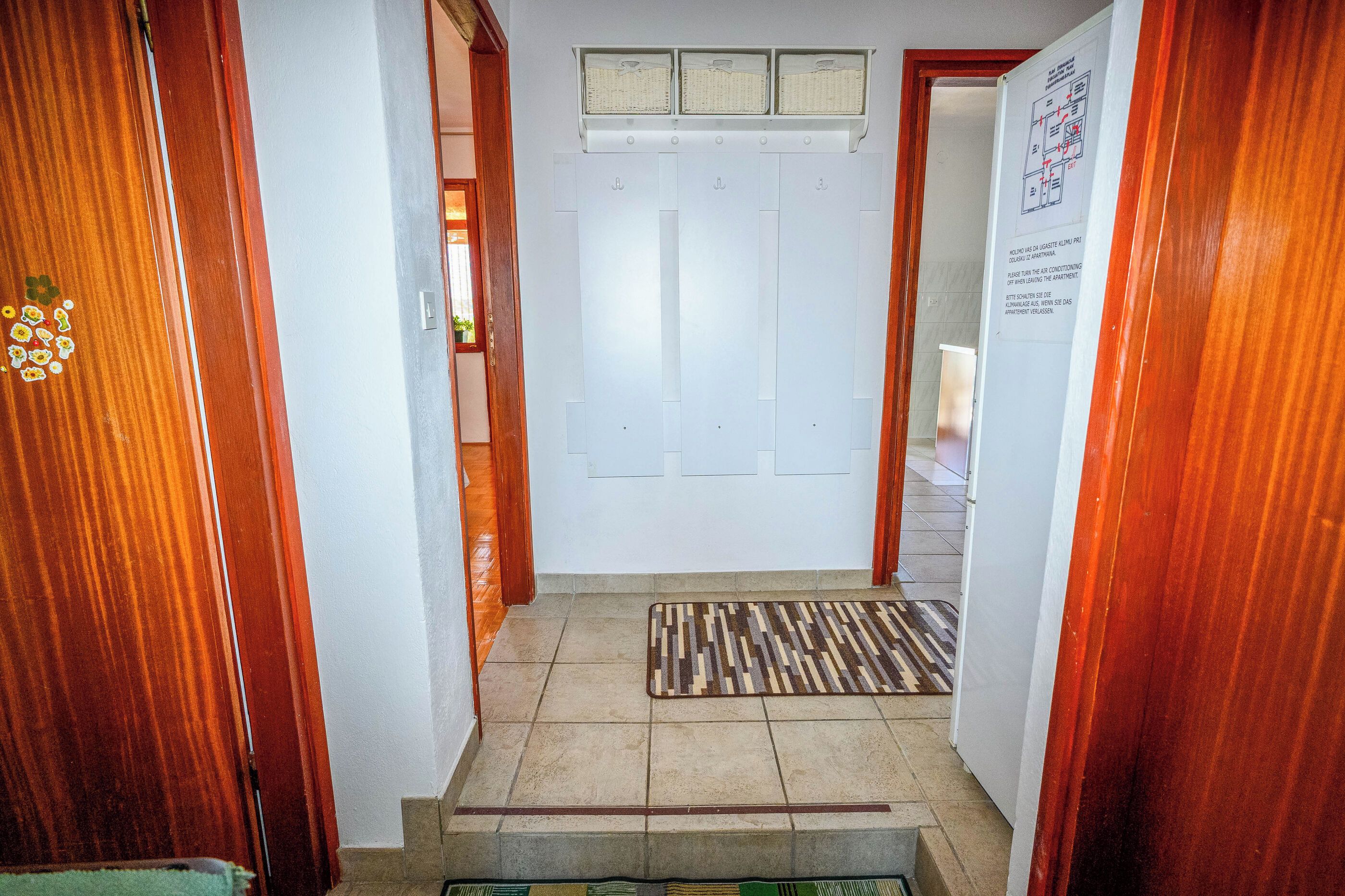 Un pasillo con una puerta de madera, una pared blanca con un aviso y una alfombra estampada.